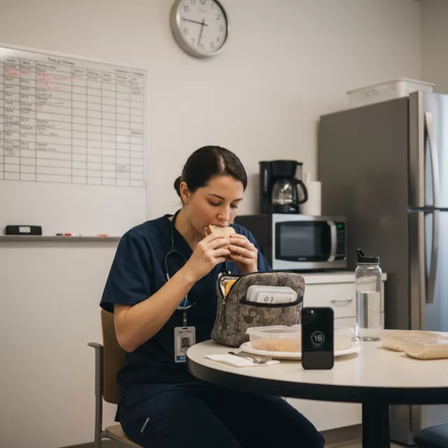 Nurse eating packed lunch quickly in hospital break room during short break