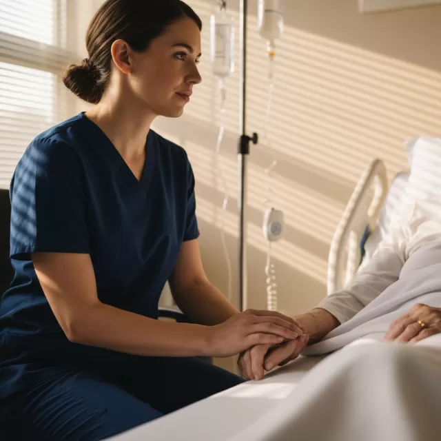 Nurse holding patient's hand at bedside in hospital room during end of shift