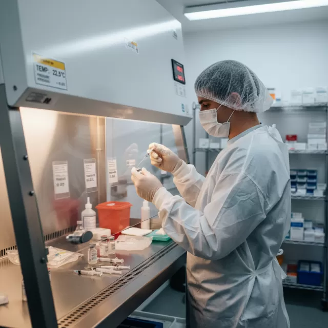 Pharmacy technician in sterile garb compounding medications in USP 797 compliant cleanroom at laminar flow hood